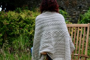 back of woman on chair with a cream aran blanket over her shouders