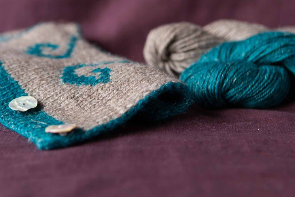 Two skeins of Nua Sport beside the Cruinne Cowl by Eimear Early on a purple linen backdrop.