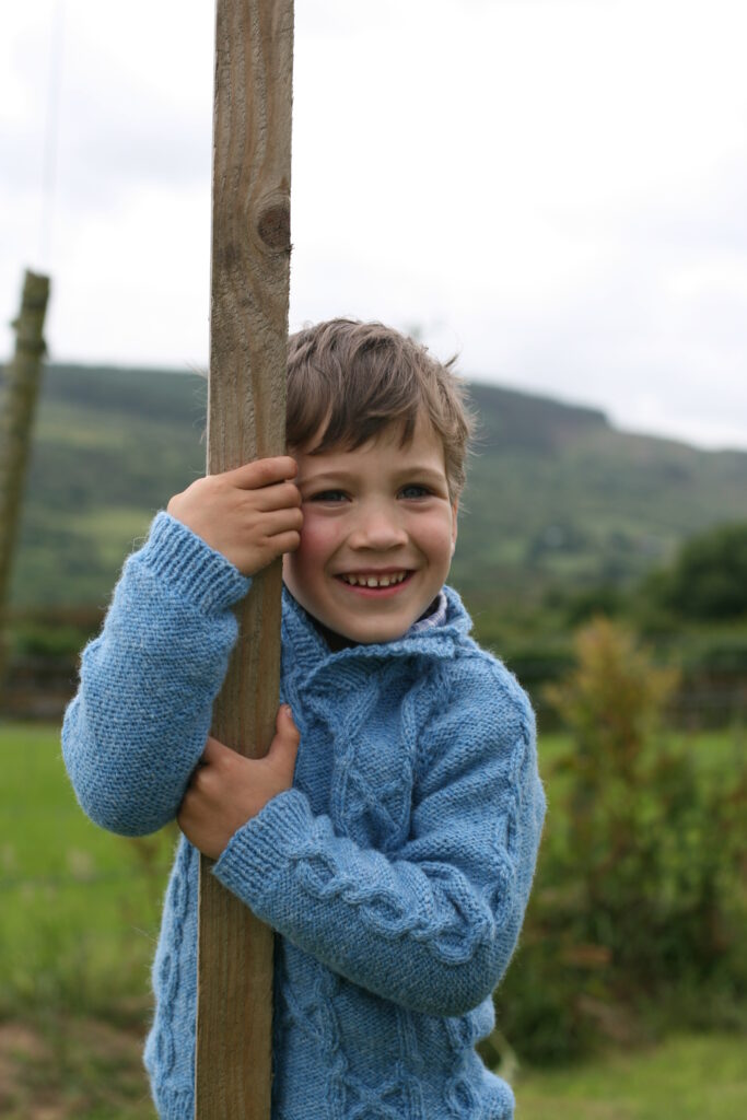 child wearing a handknit cable sweater designed by carol feller